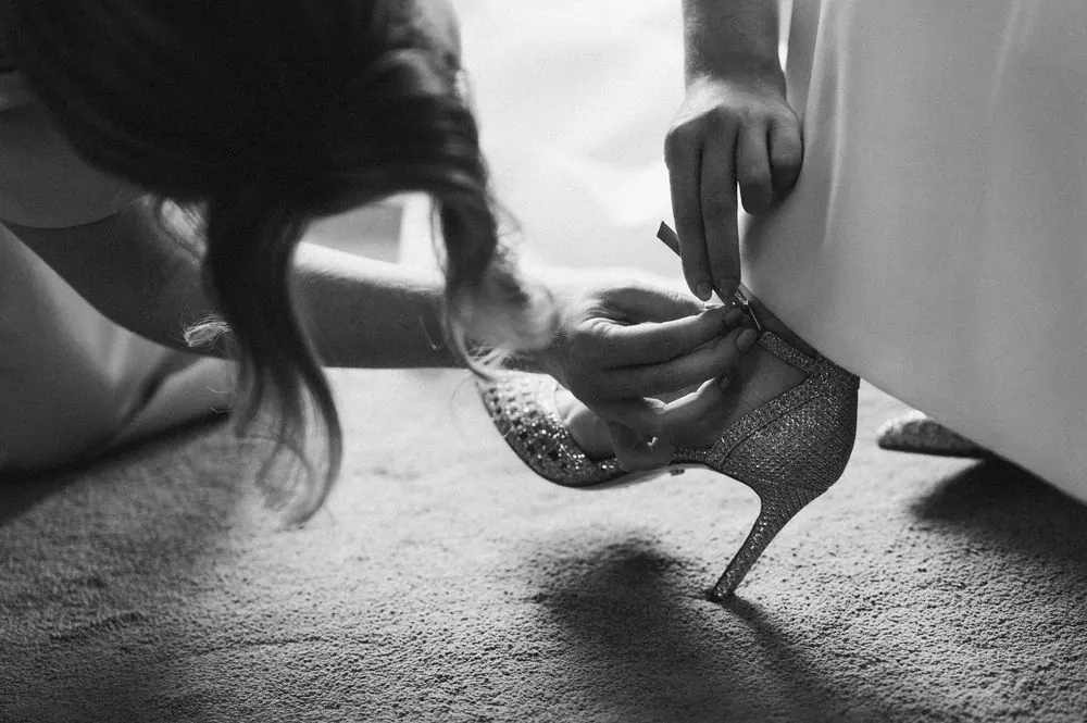 Black and white photo of a woman helping a bride put on a sparkly high heel shoe before the wedding at Boyne Hill House Estate, Co. Meath