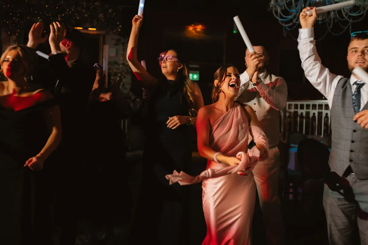 Guests dancing and celebrating at a lively wedding reception at Cabra Castle, holding glow sticks under dark atmospheric lighting.