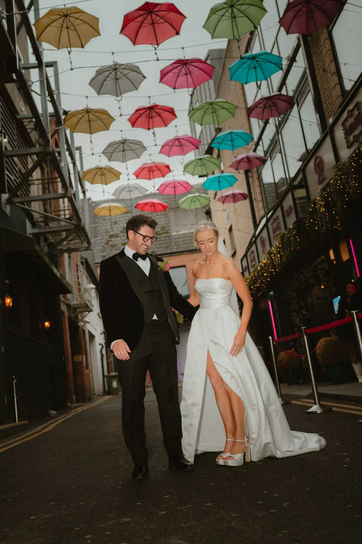 The couple walking beneath colourful umbrellas in a city lane