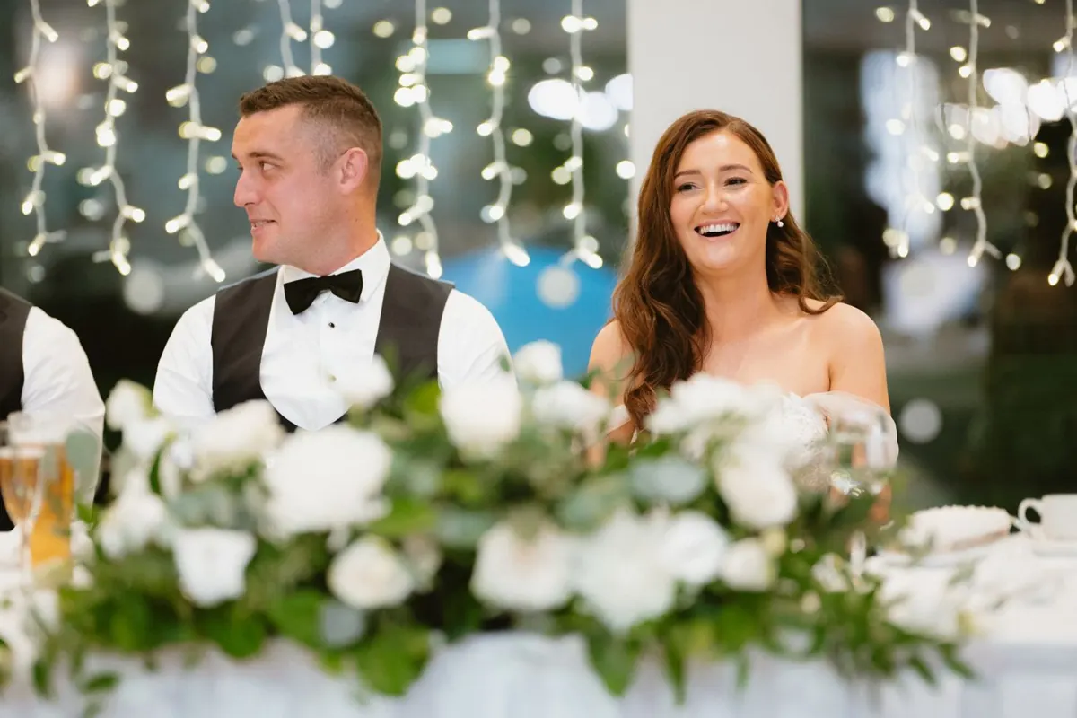 The bride laughing beside the groom at the flower-filled top table