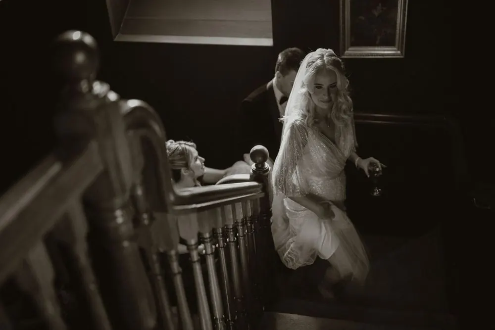 Black and white photo of a bride in a white gown and veil ascending a grand staircase on her wedding day at Boyne Hill House