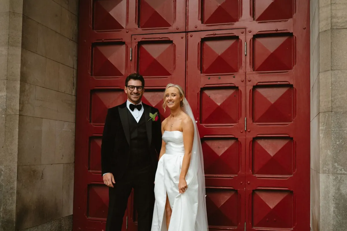 The couple standing against large red doors in the city
