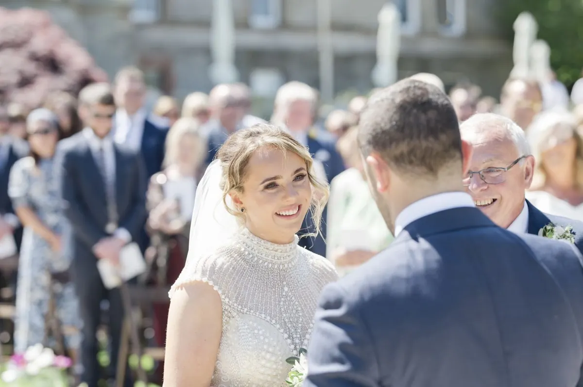 Steph smiling towards Ramon with the ceremony guests behind