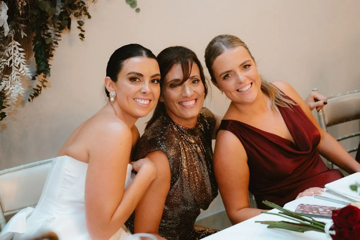 The bride smiling with two women at the reception table