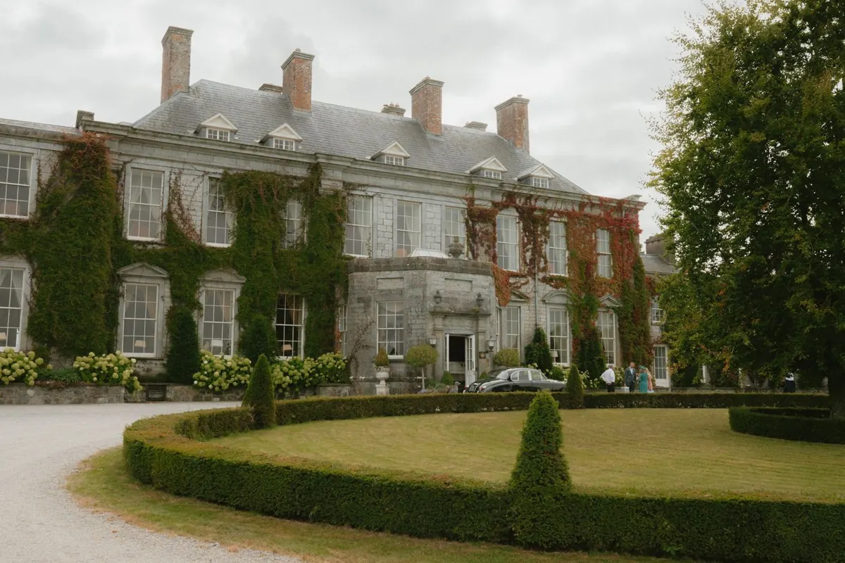 The stone house exterior beyond clipped garden hedges