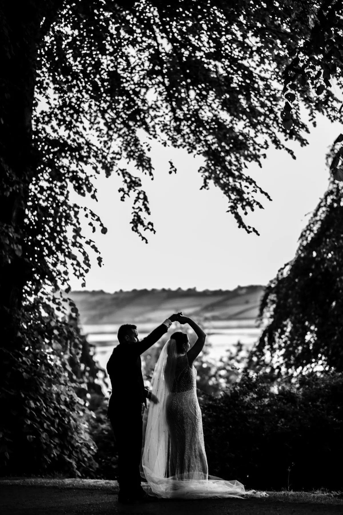 A silhouette of the couple beneath an arch of foliage
