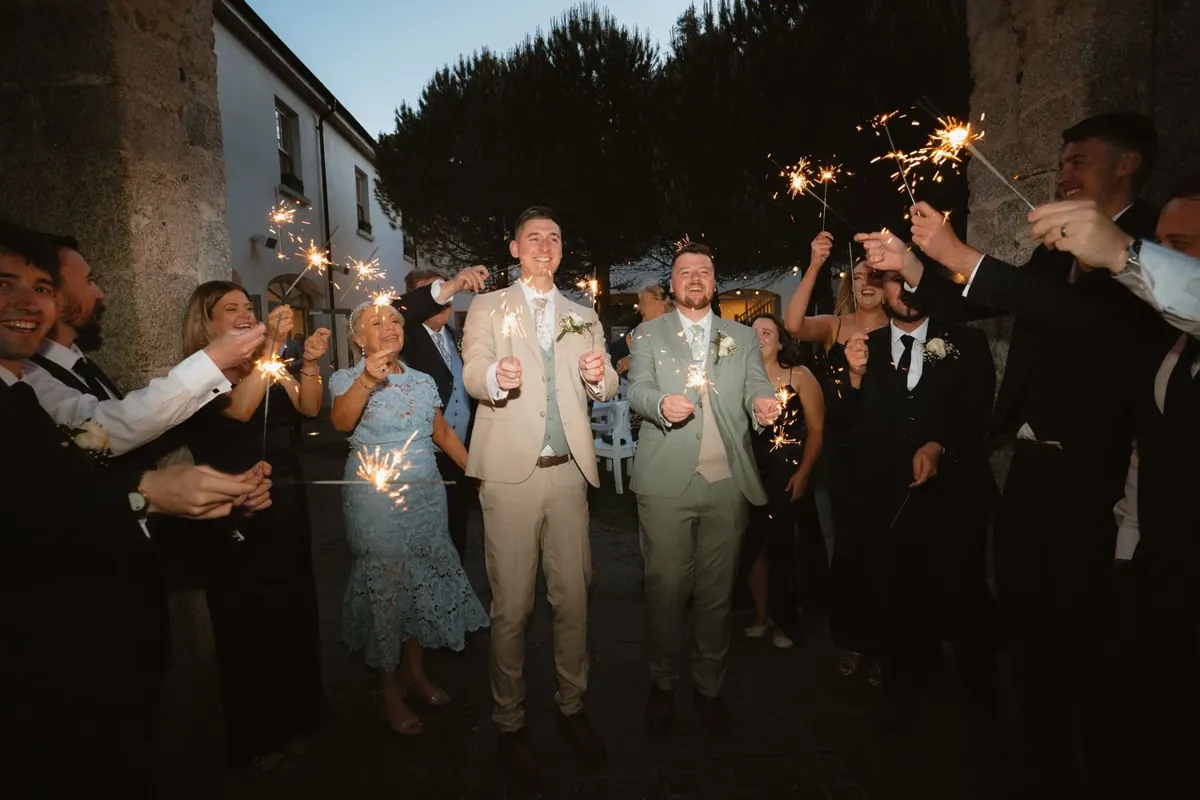 The grooms walking between guests holding sparklers after dark