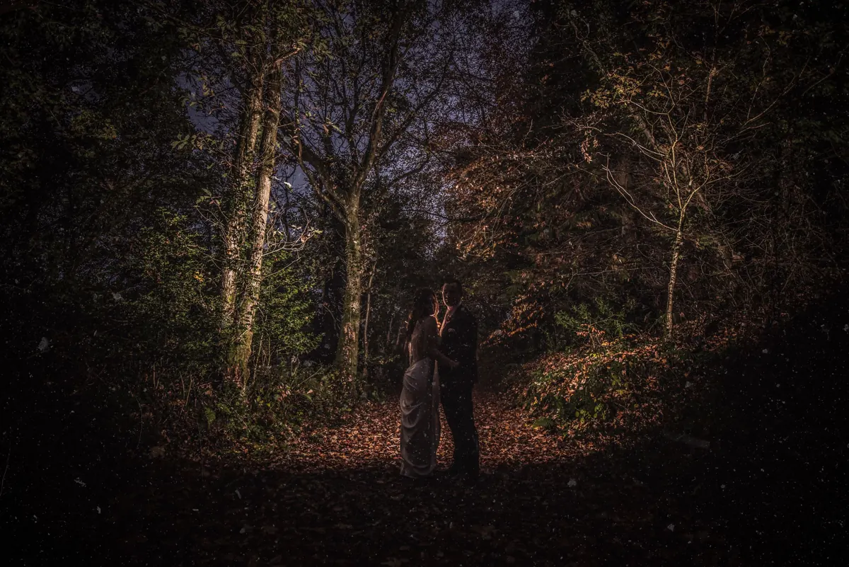 Couple embracing romantically in a dark enchanted forest at night, surrounded by trees and fallen leaves at Cabra Castle, Co. Cavan
