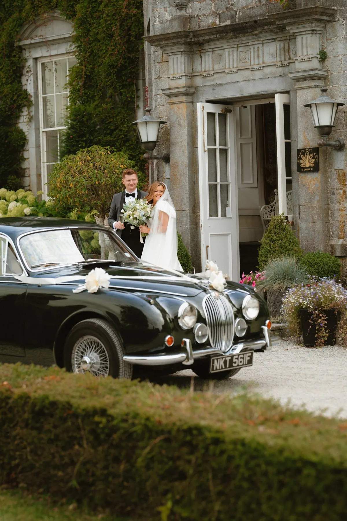 The couple beside a vintage wedding car outside the house