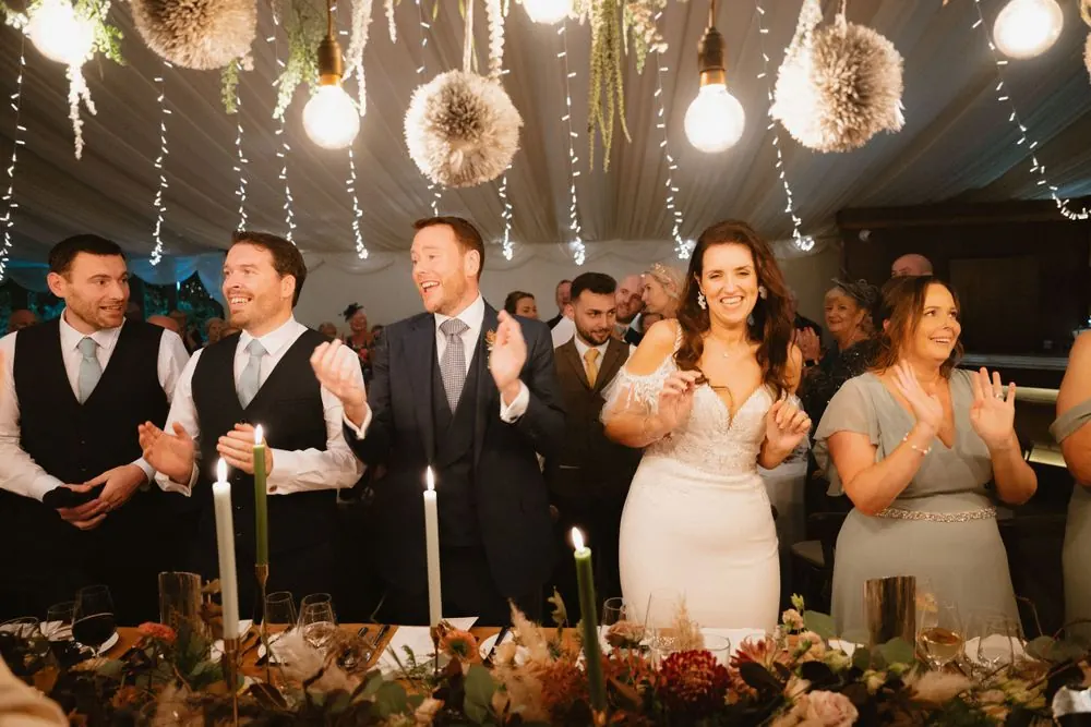Aine and John applauding with their wedding guests.