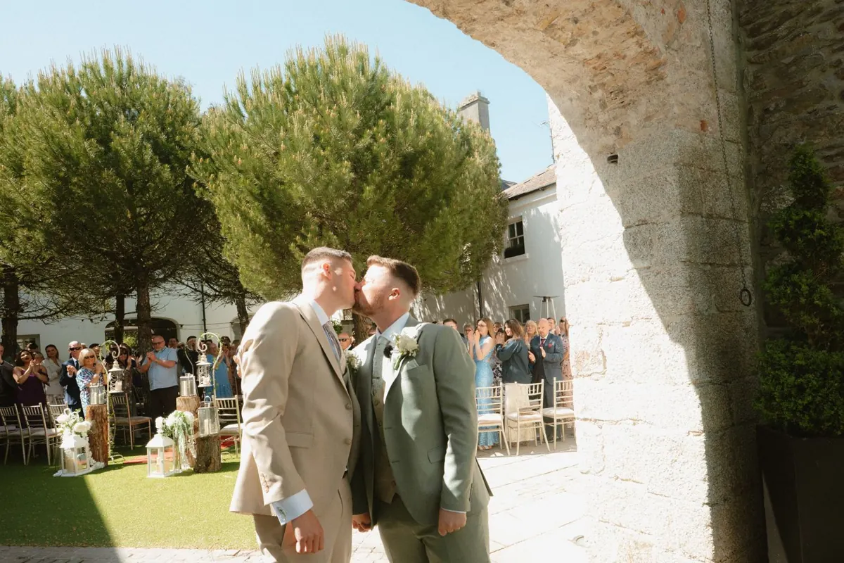 The grooms kissing beside the stone arch after the ceremony