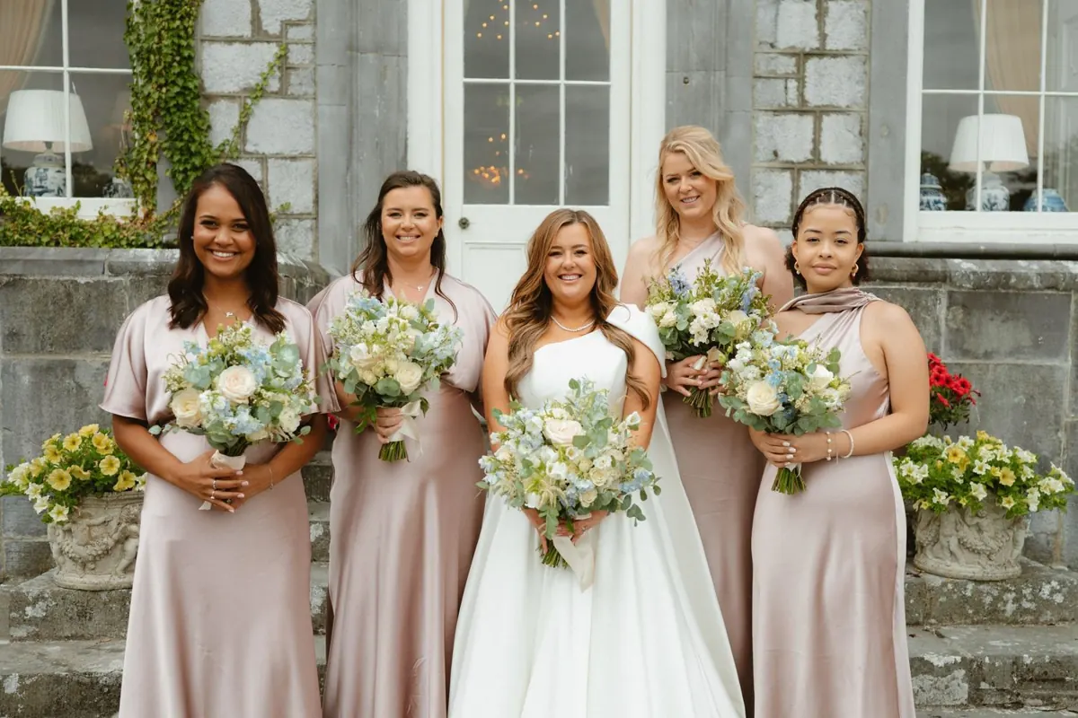 The bride with women holding bouquets in front of the house
