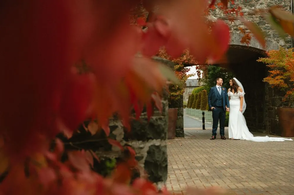Aine and John framed by autumn leaves and a stone archway.