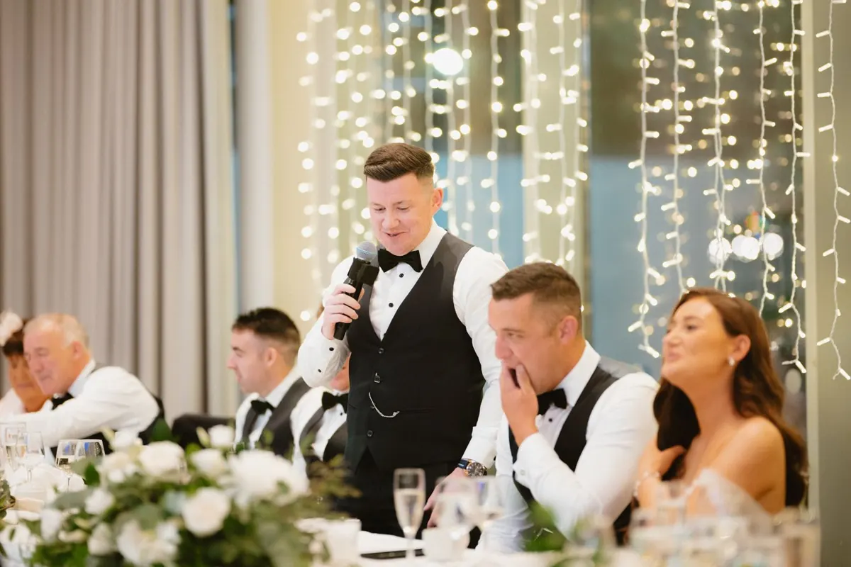 A guest giving a speech as the groom covers his face