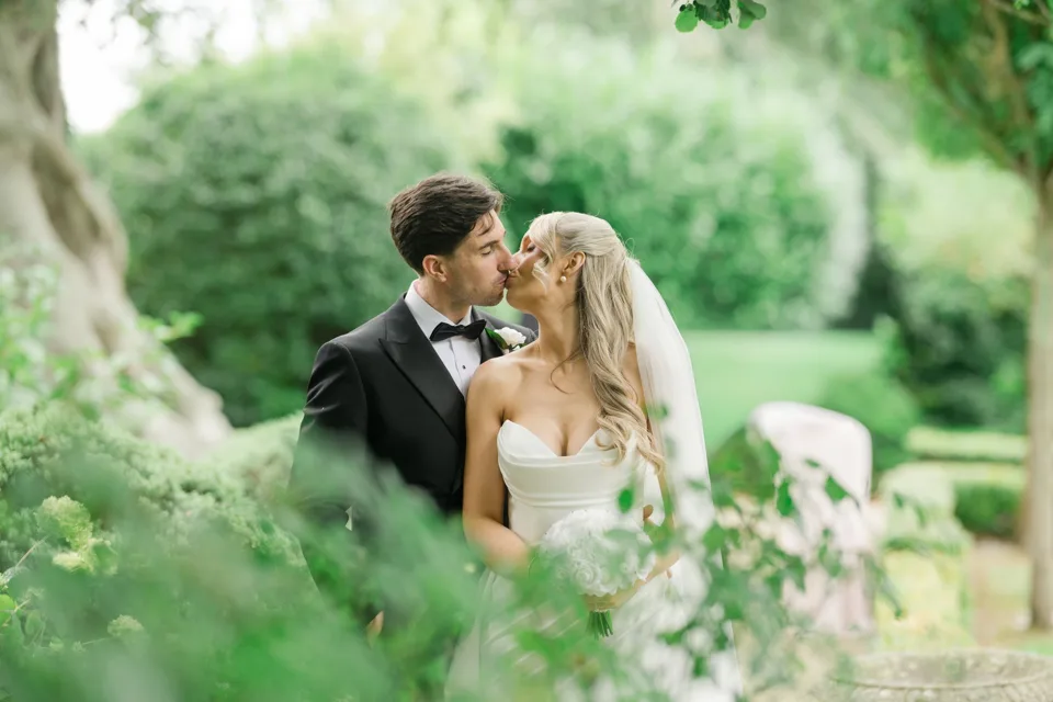 Bride and groom share a romantic kiss surrounded by lush green garden foliage on their wedding day Cliff at Lyons Co.Kildare