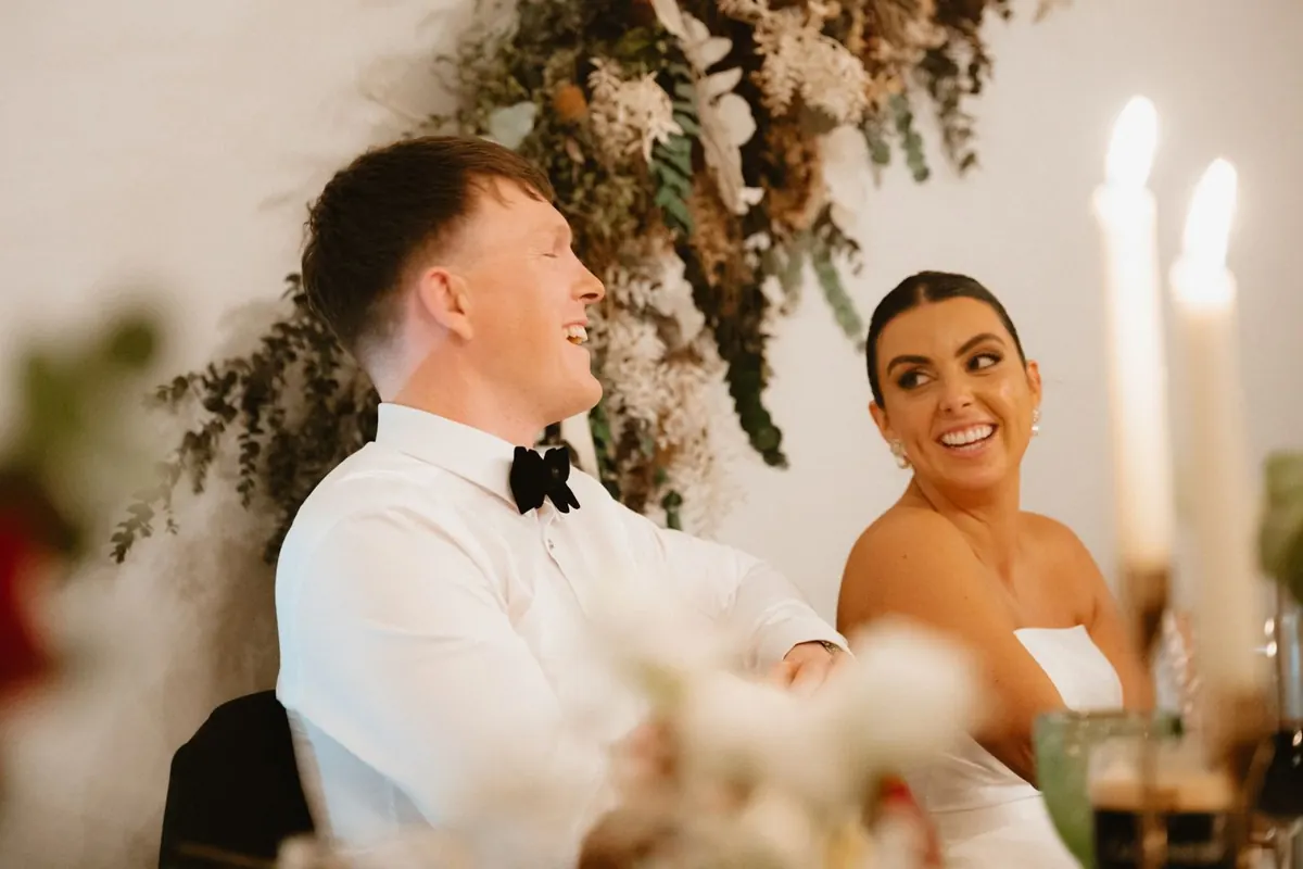The bride laughing as the groom speaks at the top table