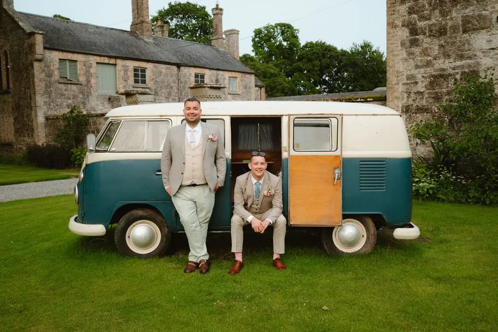 The two grooms beside a green and cream campervan in front of the house