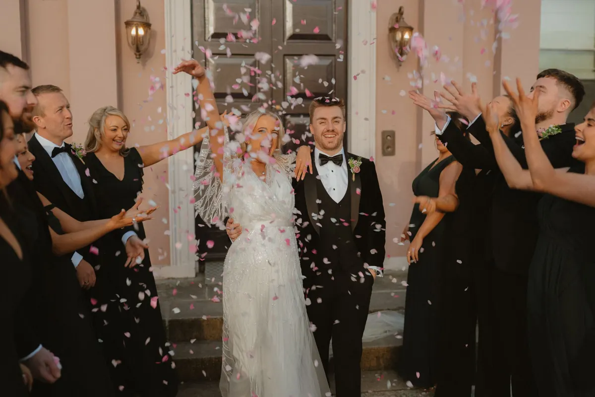 Bride and groom walk through confetti shower surrounded by wedding guests outside elegant venue doors at Boyne Hill House Estate
