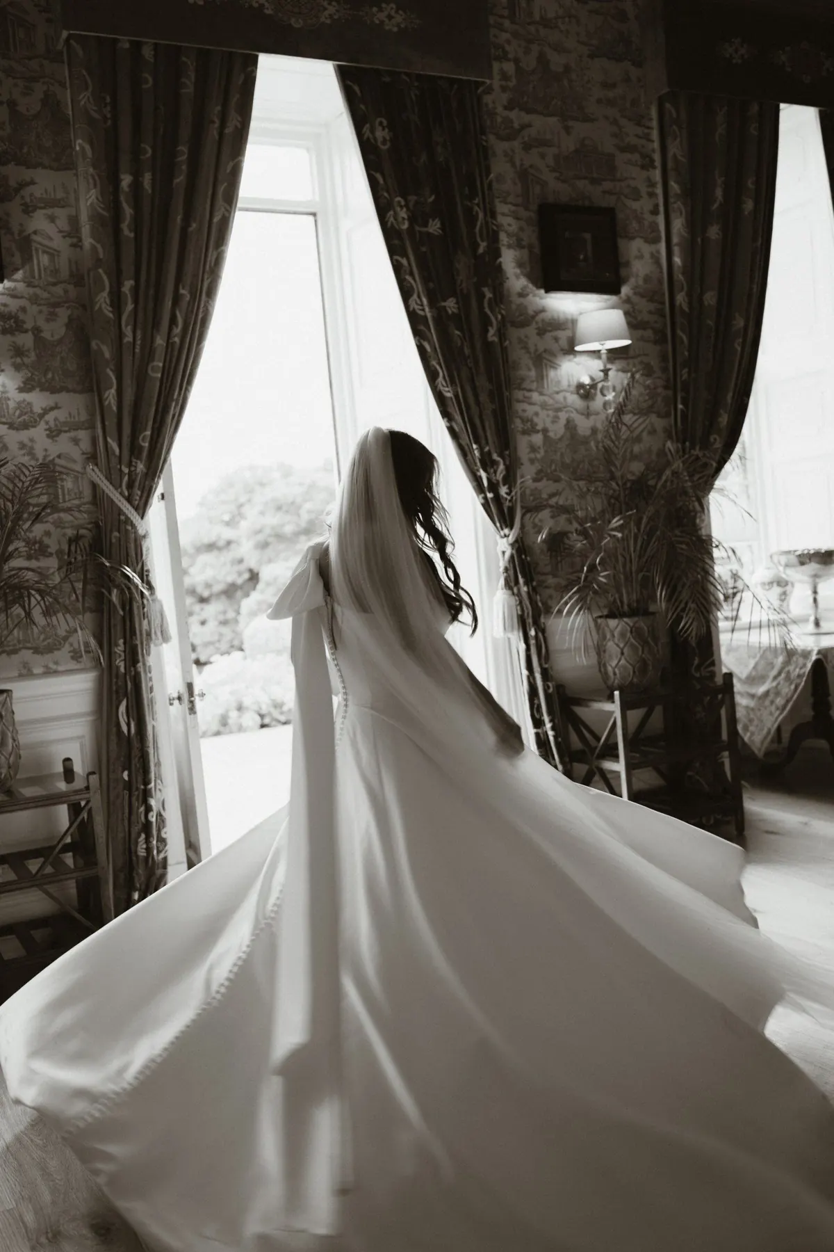 Black and white portrait of the bride and her dress beside a window