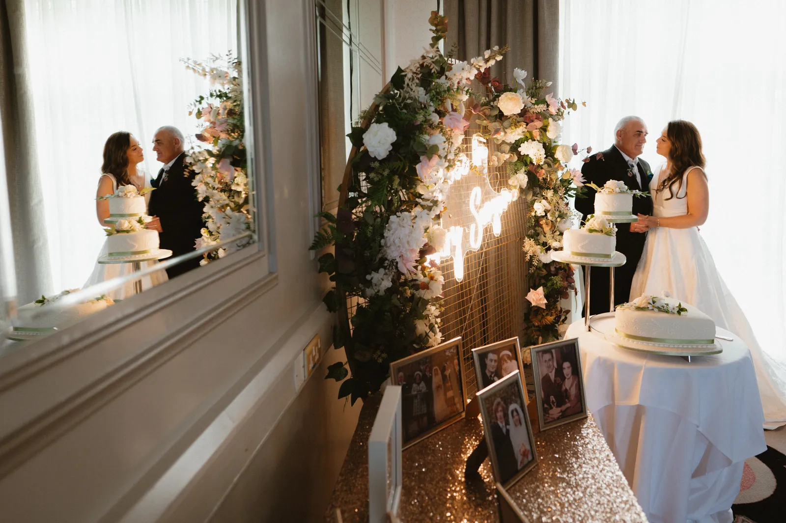 Alice and Darren beside their wedding cake, reflected in the reception-room mirror