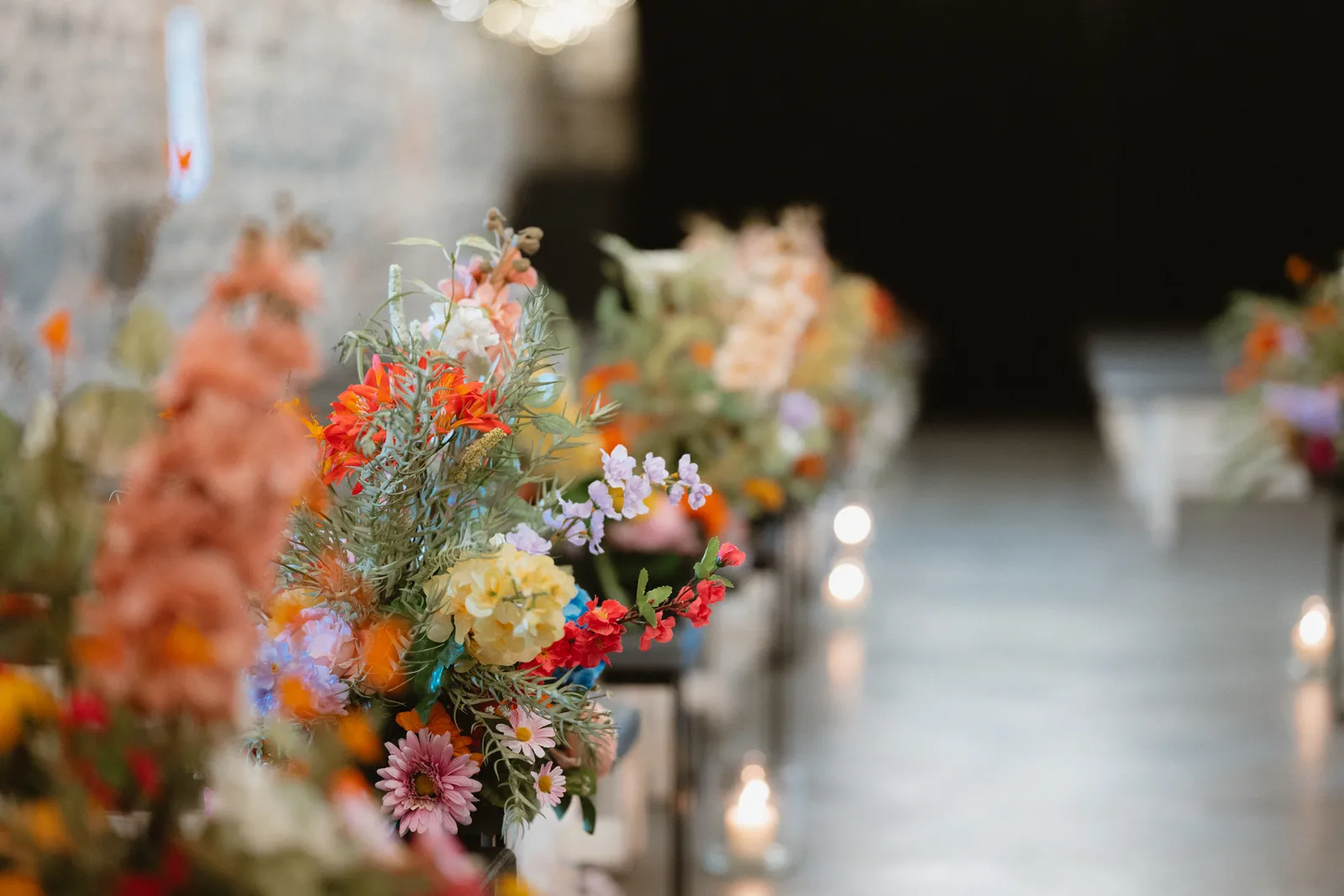Bright orange, pink and yellow flowers line the aisle inside the stone ceremony barn.