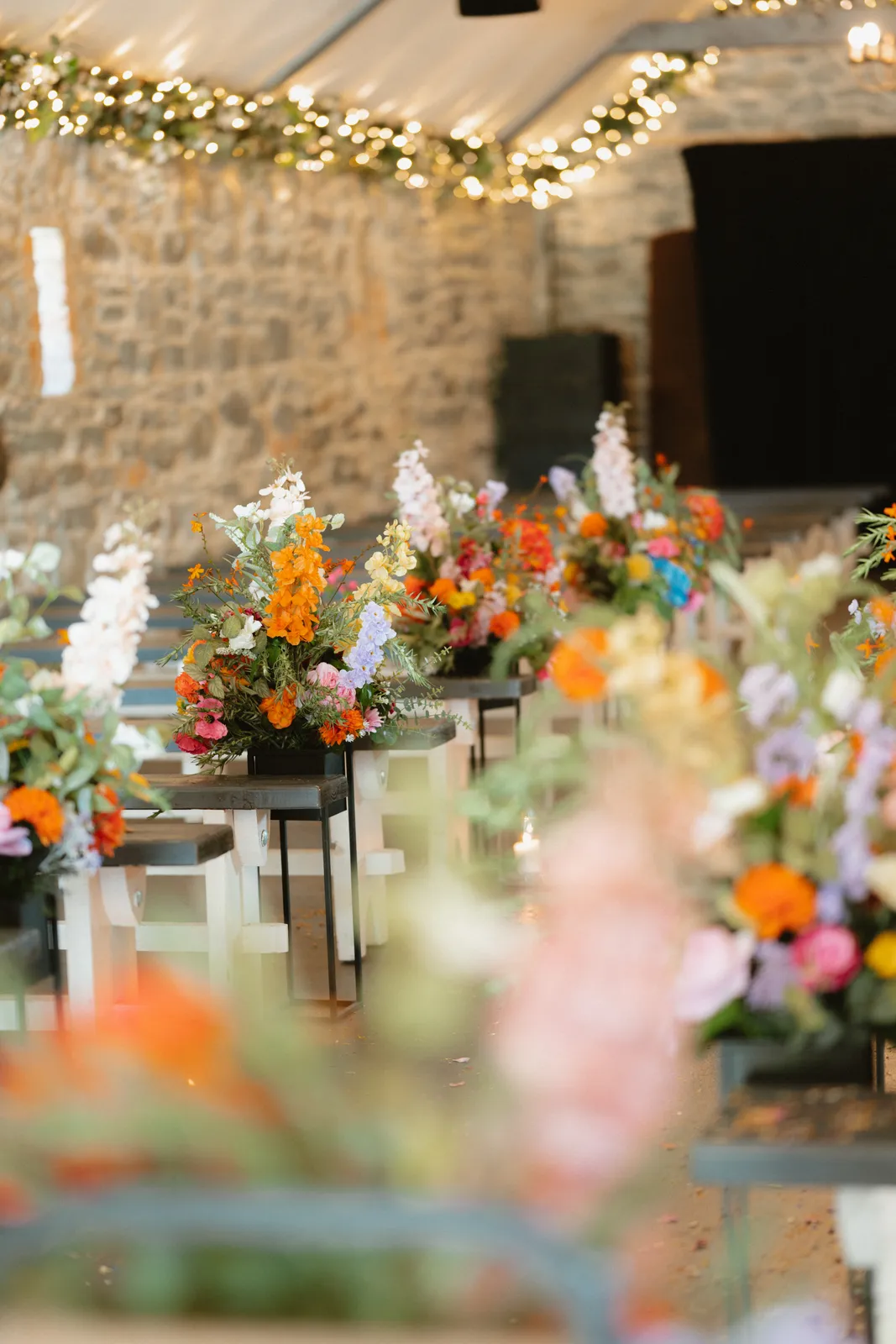 Colourful flowers on tall stands line the stone ceremony room beneath strings of lights.
