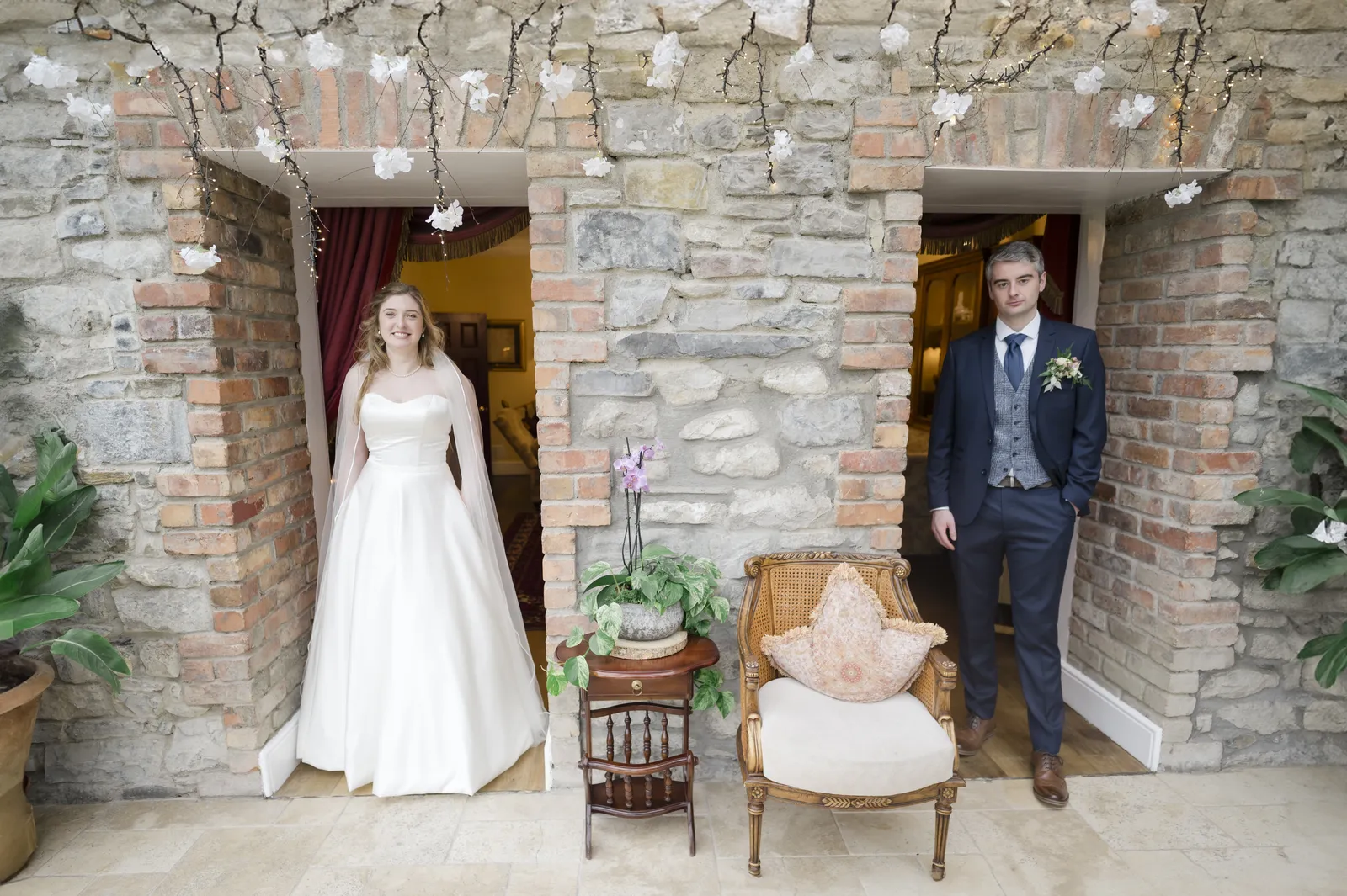 Ashling and Shaw stand in neighbouring stone doorways with a small table and chair between them.