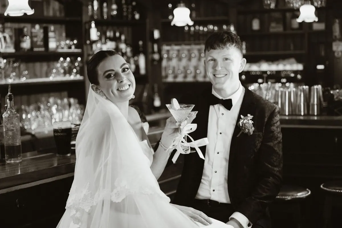 Black and white photograph of the couple raising their glasses at the bar