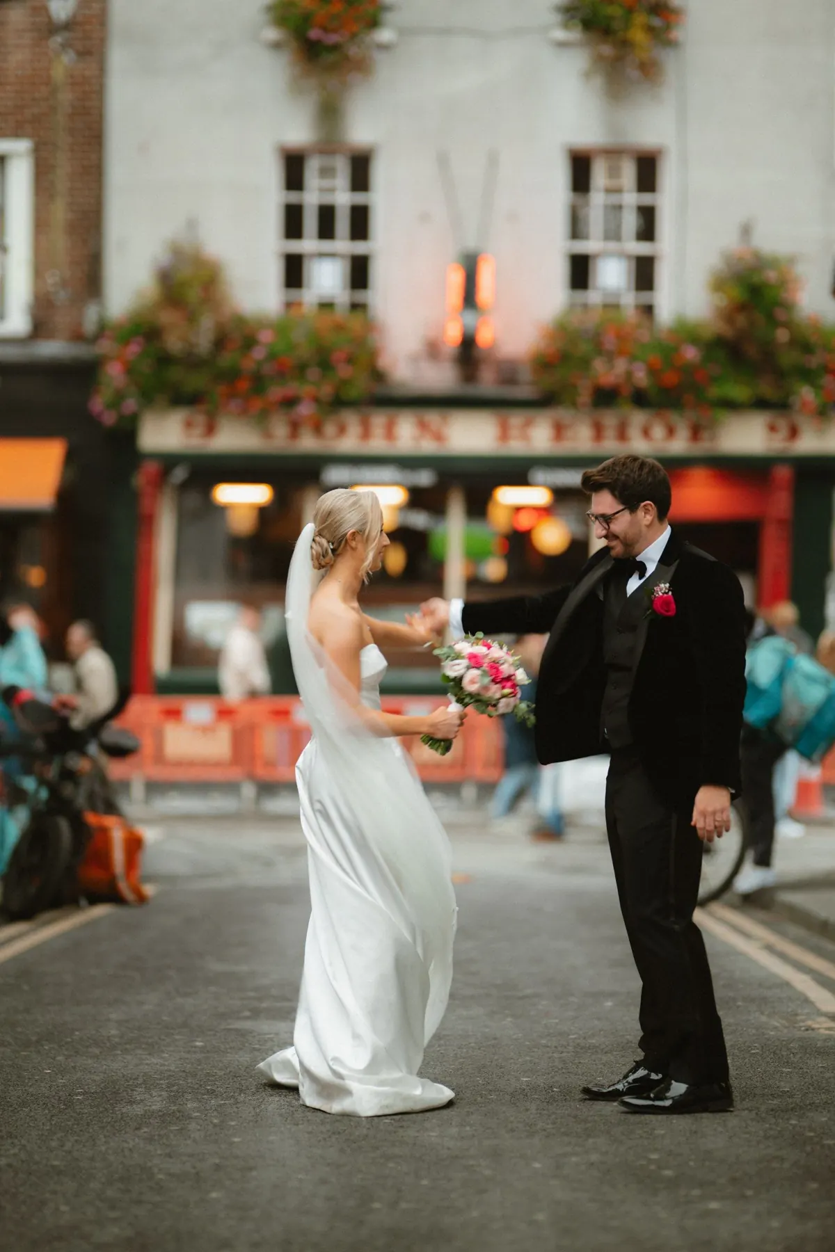 The bride raising her bouquet on a city crossing beside the groom