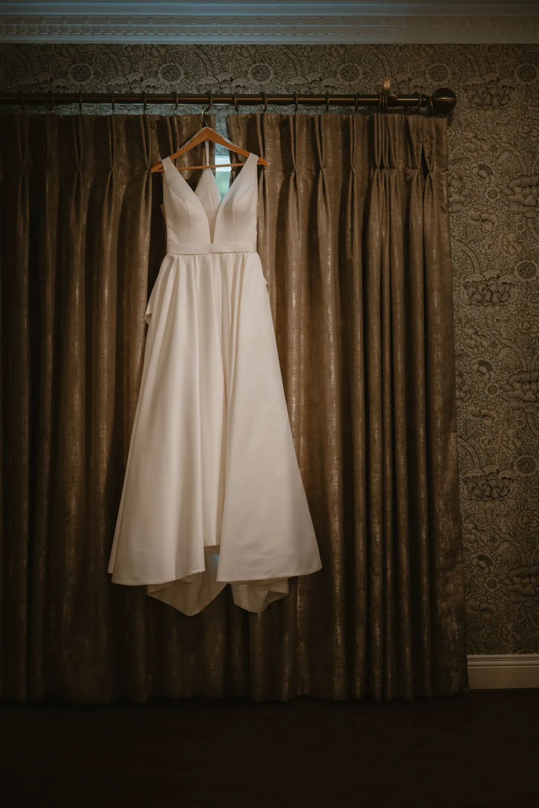 The wedding gown hanging against curtains