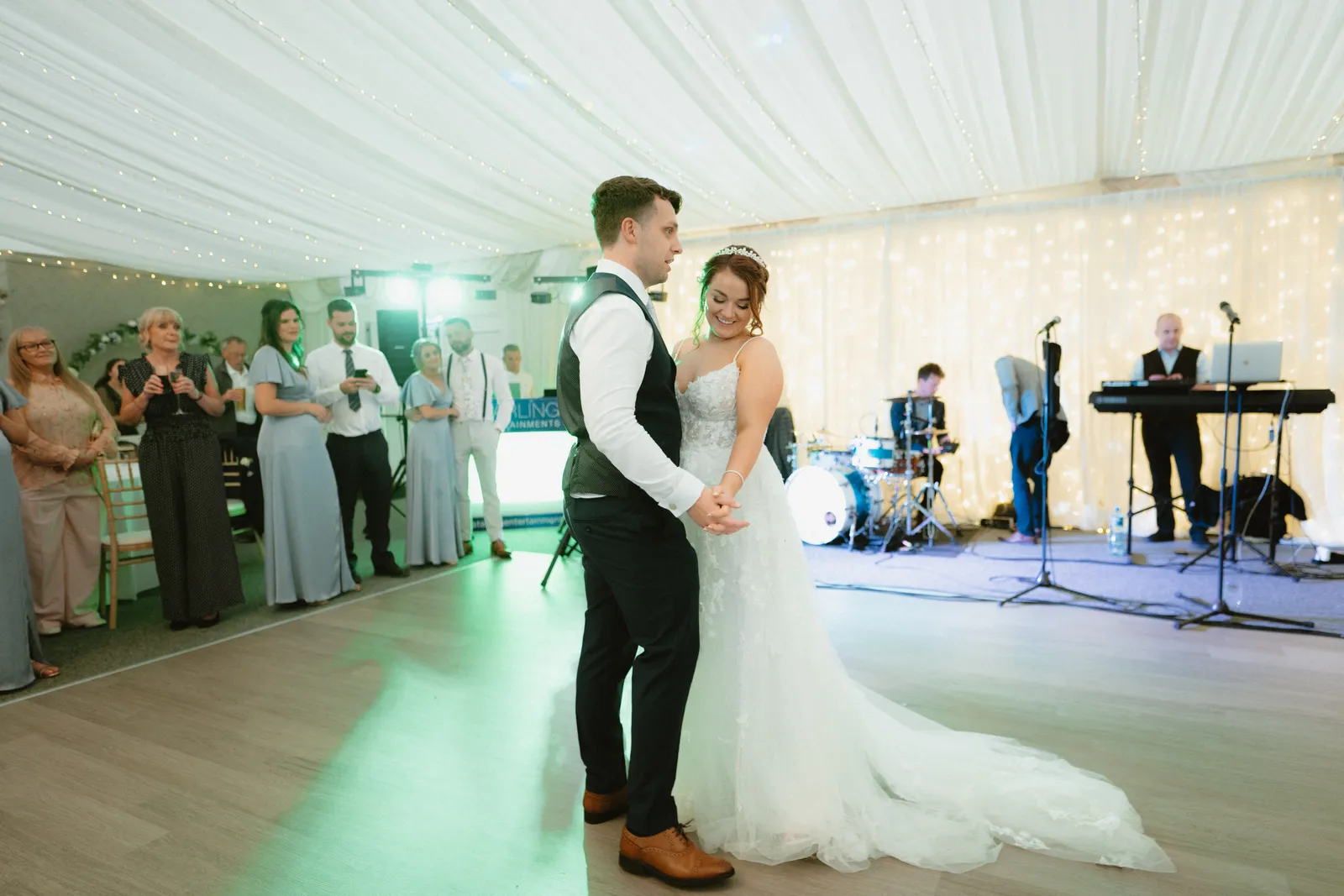 Claire and Will dance beneath the draped ceiling as guests watch and the band plays behind them.
