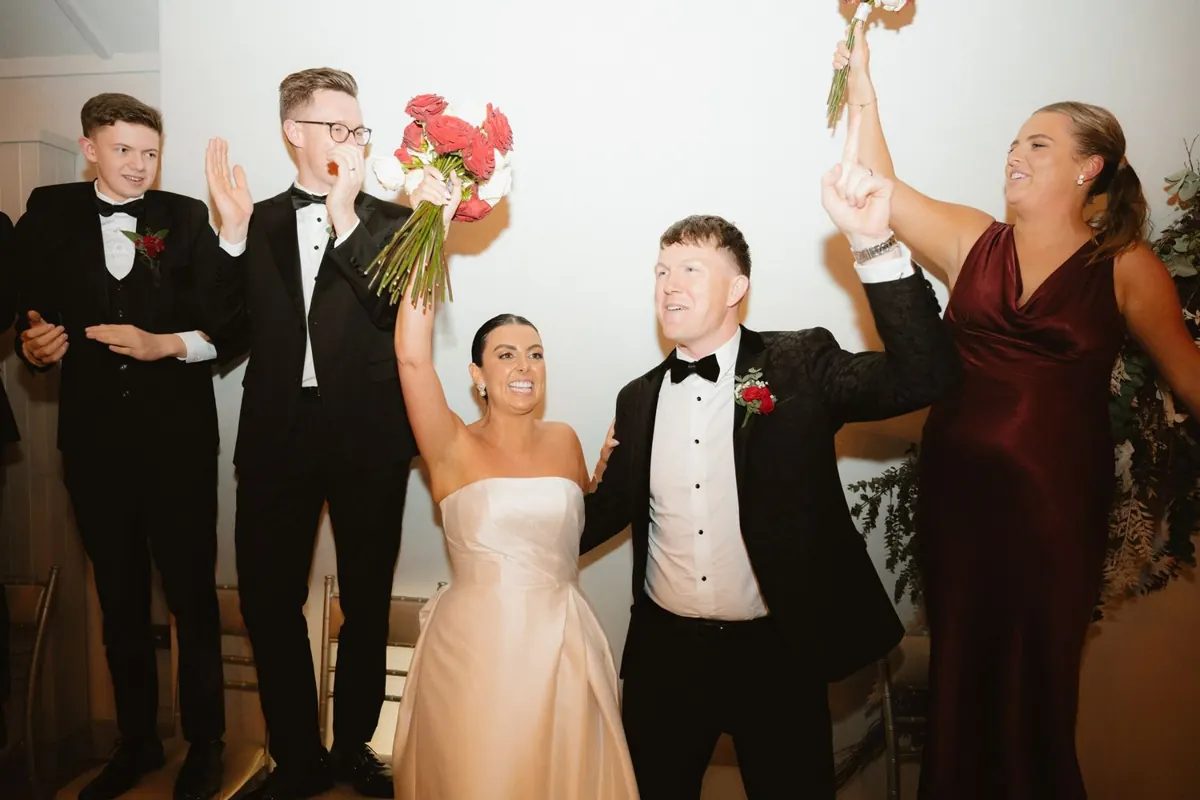 The couple celebrating with guests holding the bouquet and glasses aloft