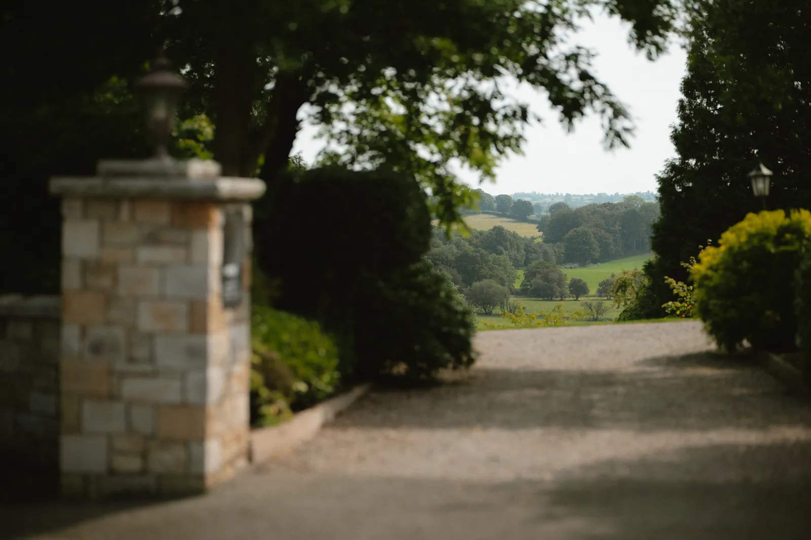 A garden path at Corick House opens between a stone pillar and clipped shrubs towards the countryside.