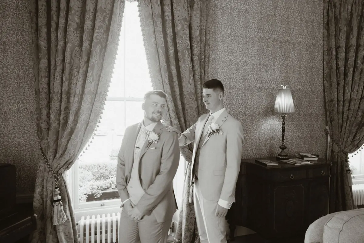 Black and white portrait of the grooms beside the tall window