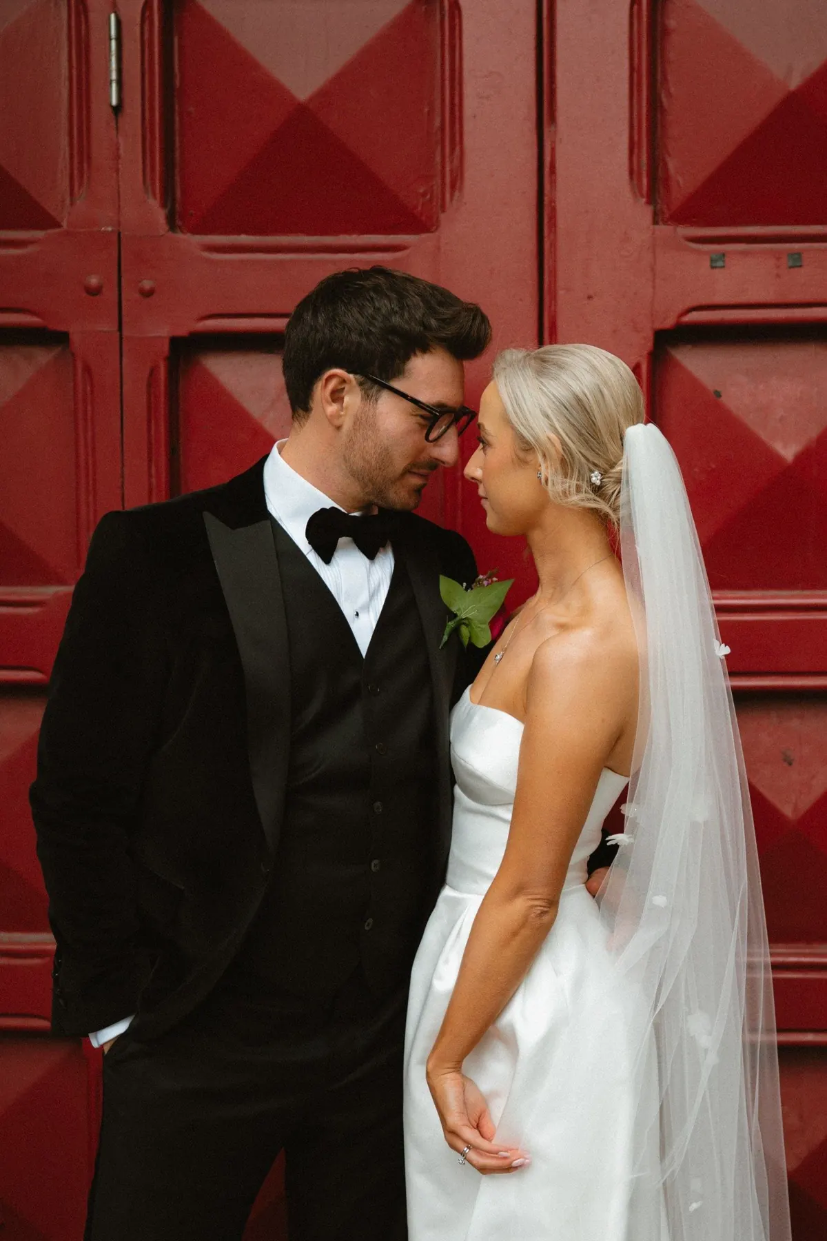 The couple kissing in front of large red city doors