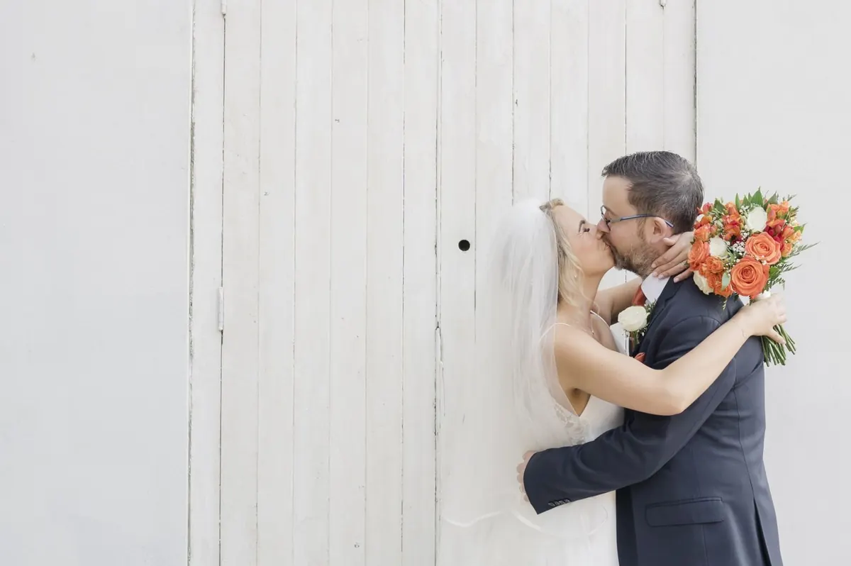 The couple sharing a kiss beside the pale wooden doors