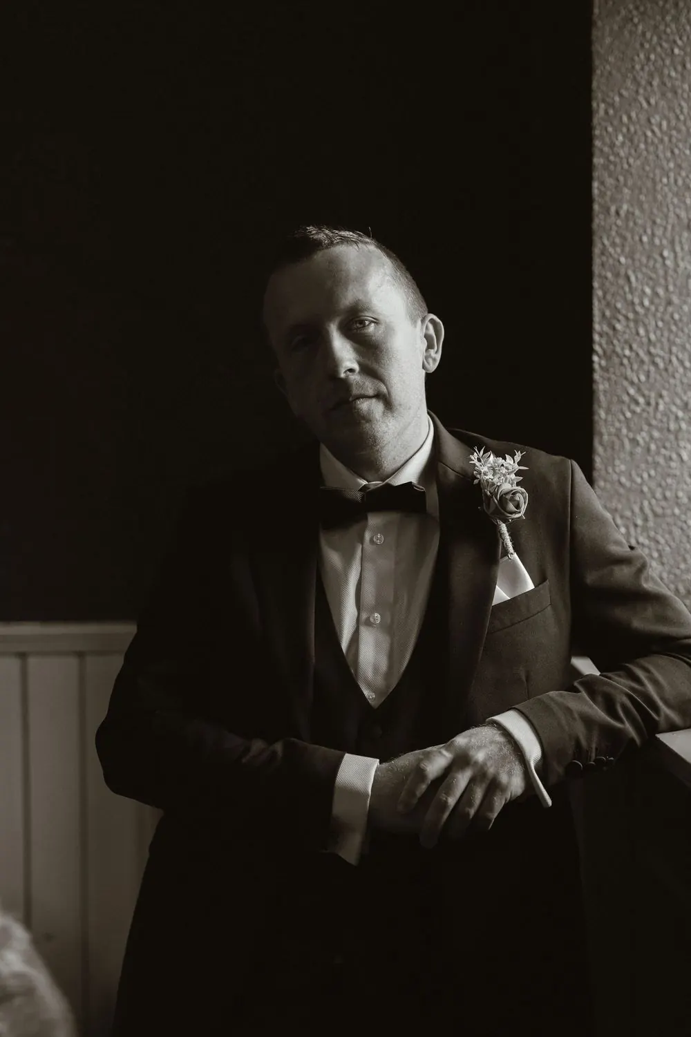 Black and white portrait of a groom in a tuxedo with boutonniere, posing in dramatic lighting at Boyne Hill House Estate