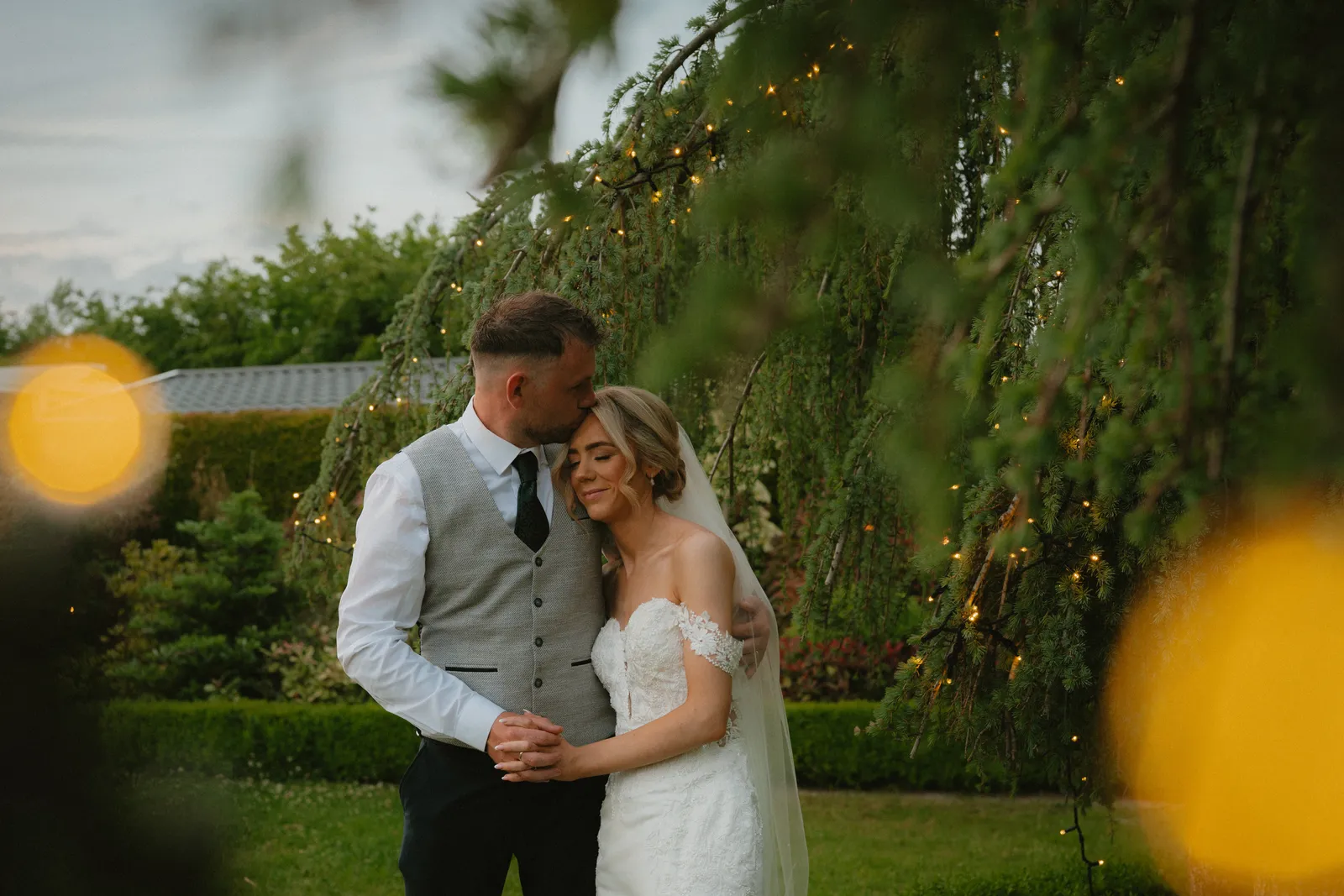 Hazel and Luke beneath hanging lights in the gardens at Clanard Court
