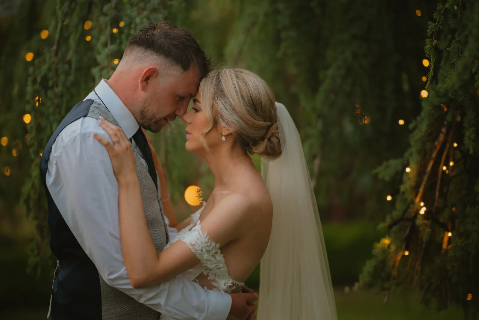 Hazel and Luke standing close beside garden lights