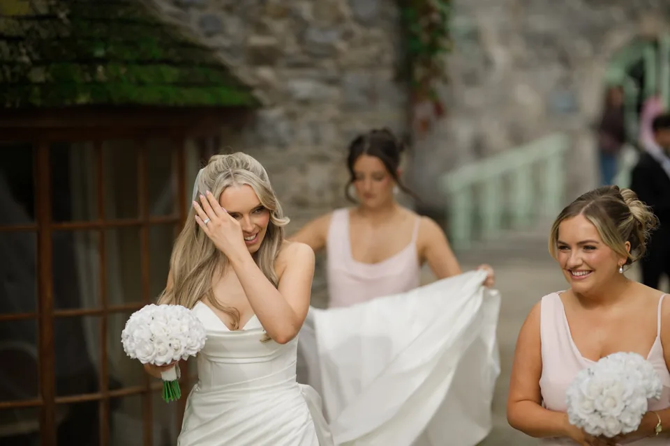 Bridesmaids laugh as they help with the dress outside.