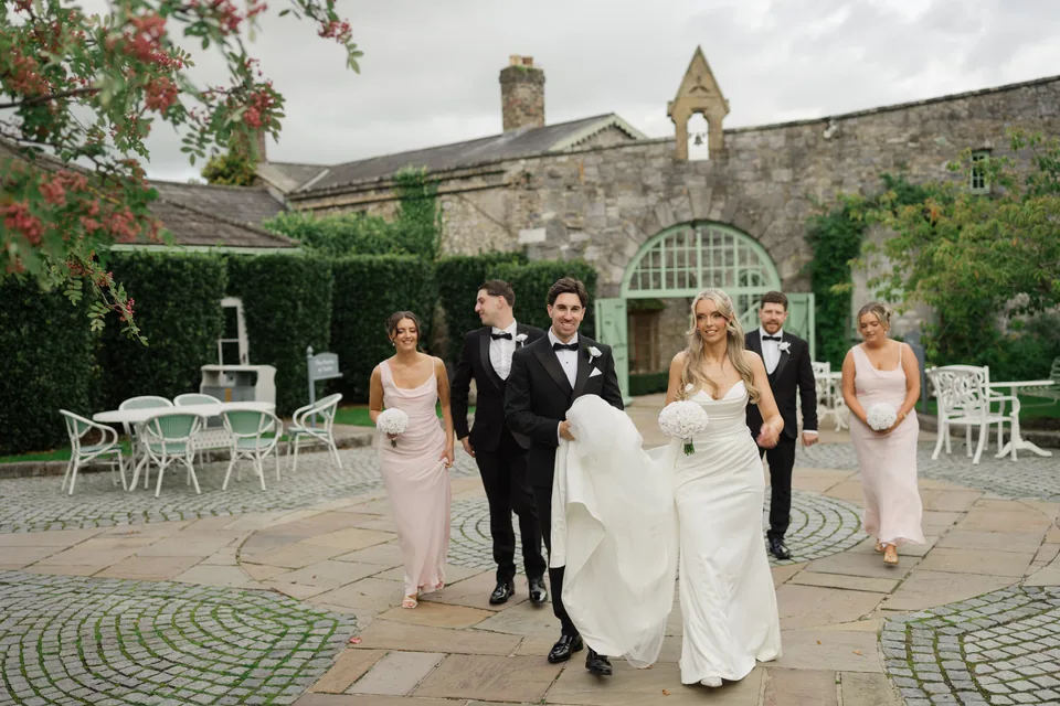 Wedding party walks through the courtyard with the venue behind.