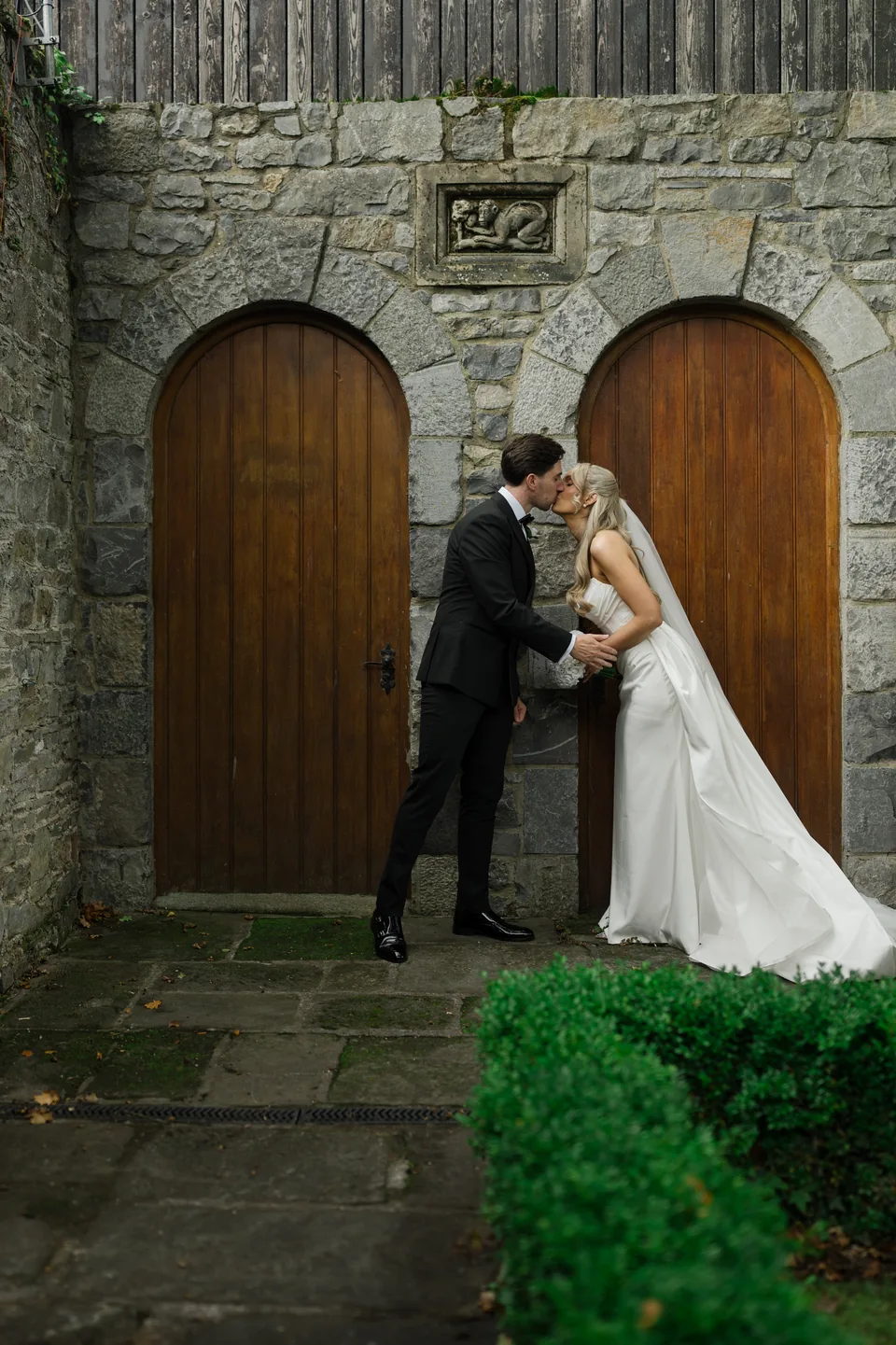 The couple shares a kiss beneath the stone arch.