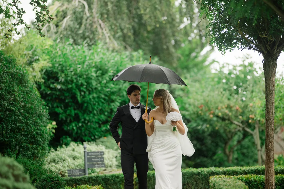 The couple beneath an umbrella, surrounded by deep green foliage.