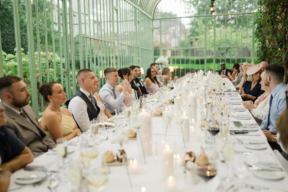 Long table and glass roof establish the wedding meal setting.