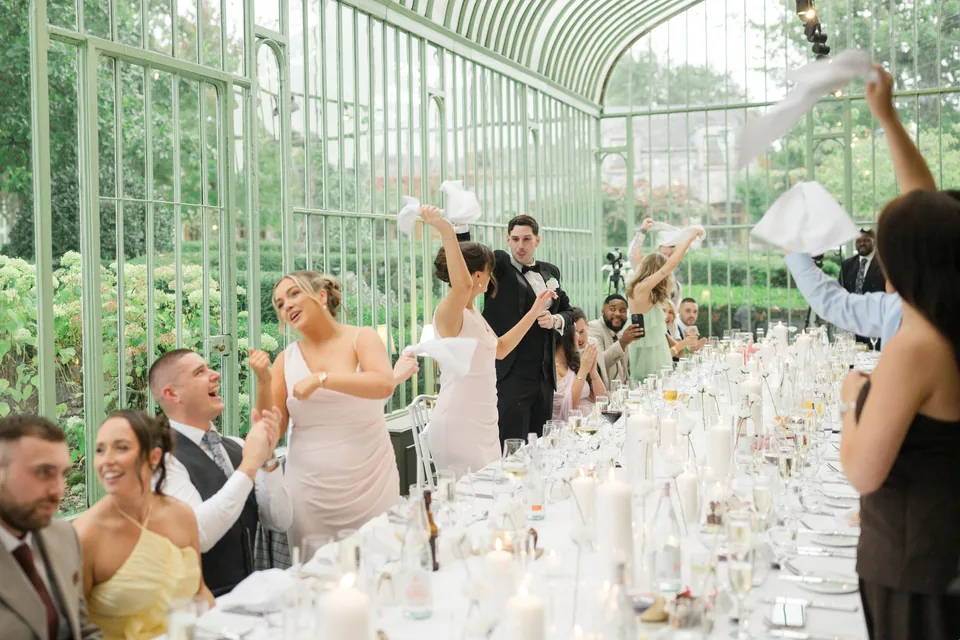 A wide celebration as the couple arrives at the long table.