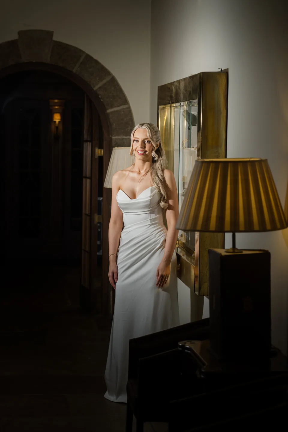 Warm lamplight and dark stone arches frame an evening bridal portrait.