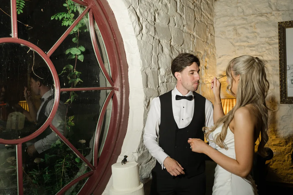 Holly and Jay cutting their wedding cake beside the round window.