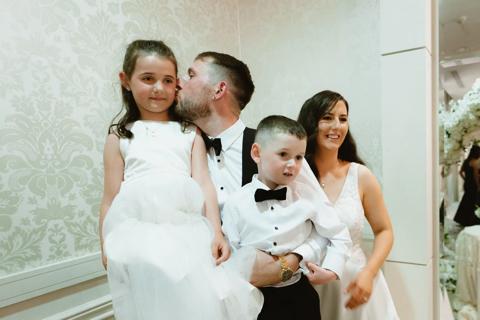 Kerstin and Cian pose with two children against a pale patterned wall.