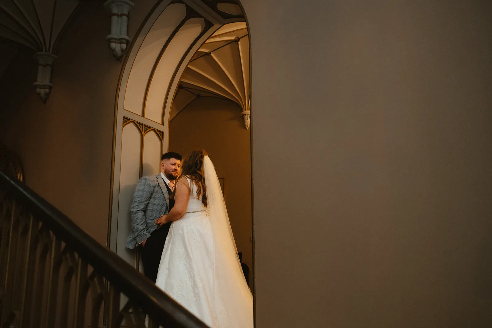 Leah and Keelan stand together beneath an arch on the castle stair landing.