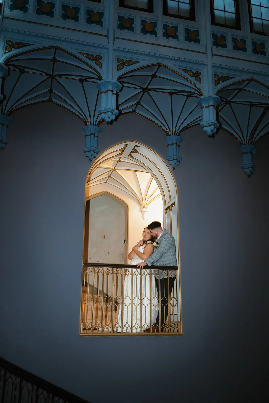 Leah and Keelan kiss in an illuminated pointed arch on the blue painted castle stairwell.